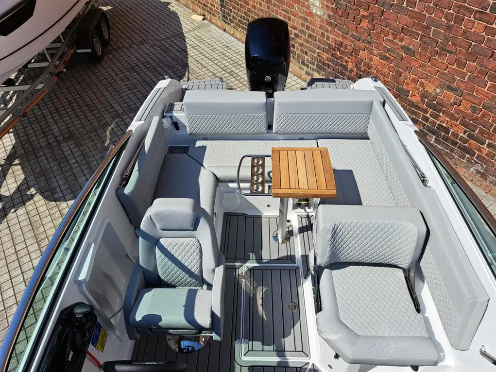 Top view of a stylish boat interior featuring grey quilted seating and a wooden table, with a motor in the background.